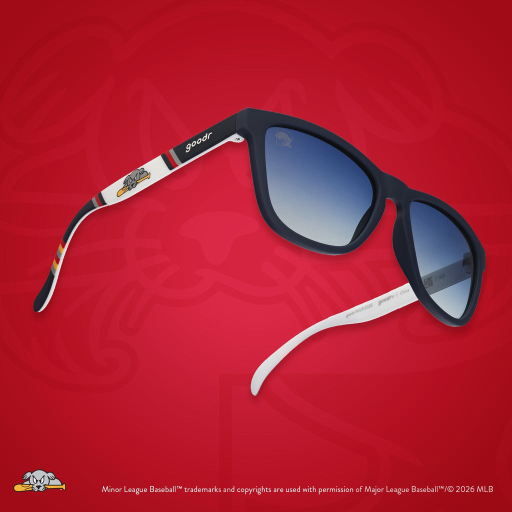 Three-quarter angle view of sunglasses. Dark blue frames w/ Sea Dogs logo on temples + blue gradient lenses.