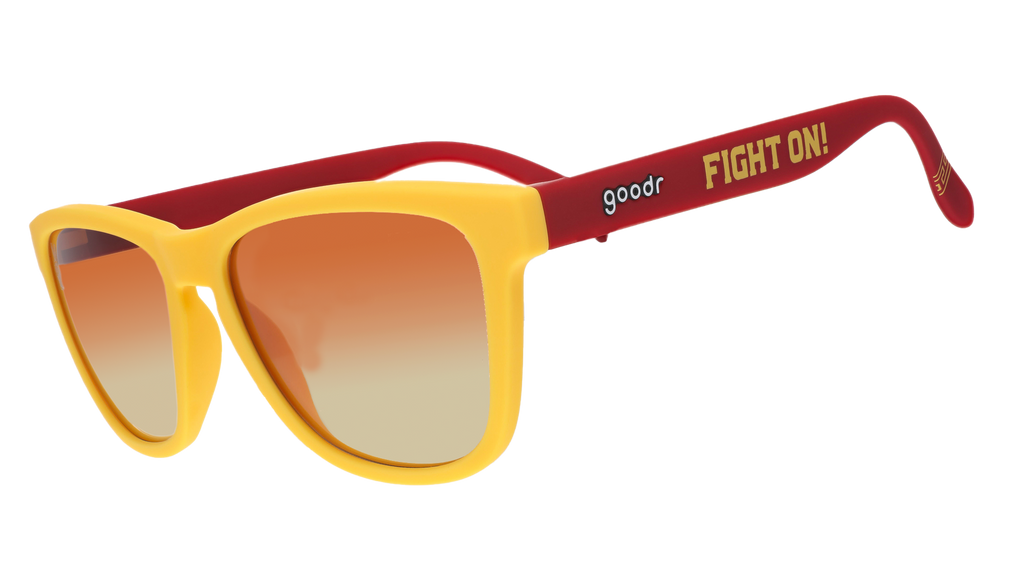A pair of sunglasses with bright yellow frames and red arms, featuring the words "Fight On!" in bold yellow text on the side. The lenses have a gradient from orange to light.