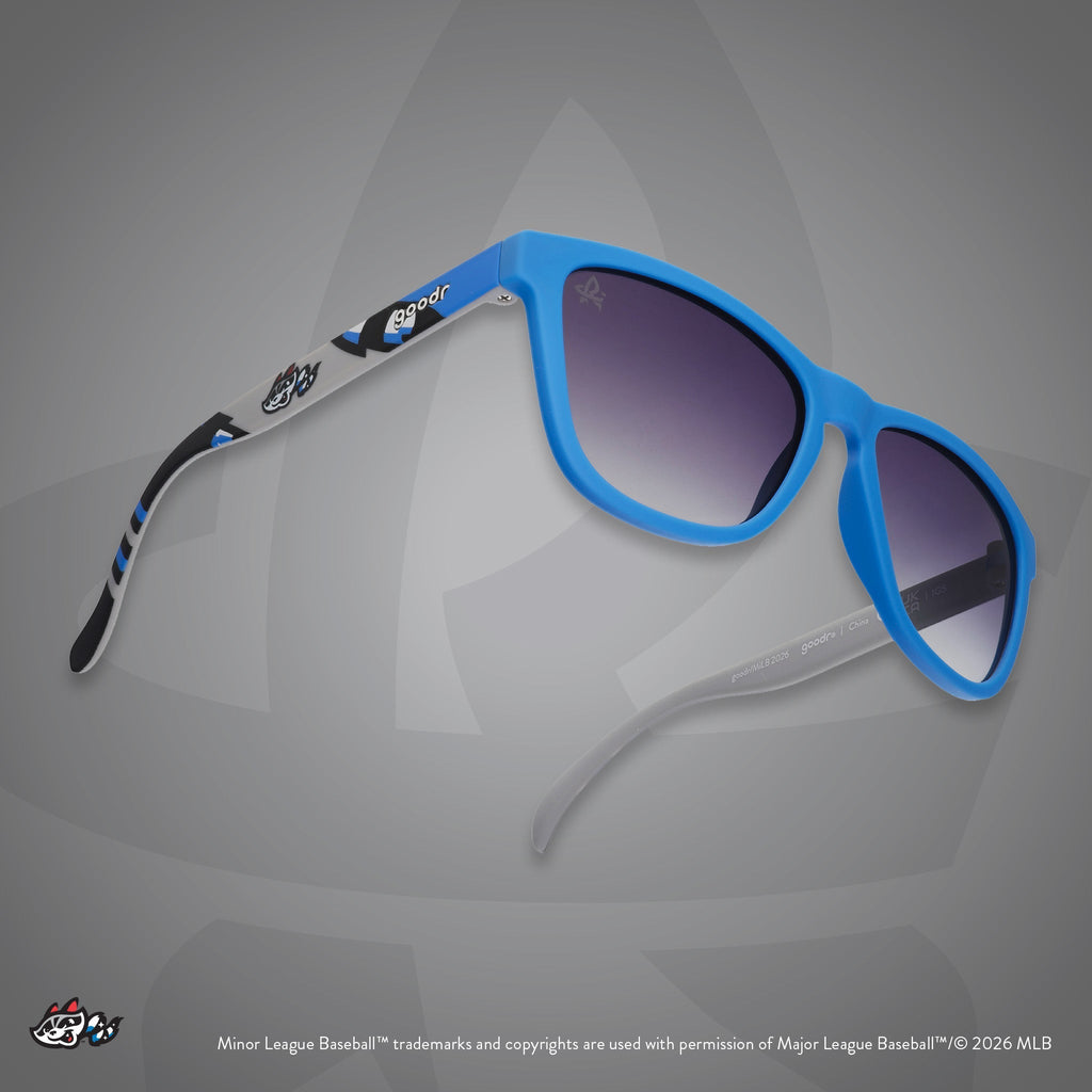 Three-quarter angle view of sunglasses. Blue frames w/ Trash Pandas logo on temples + black gradient lenses.