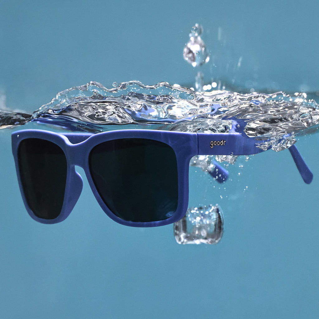 Three-quarter angle view of dark blue sunglasses with dark blue lenses floating in the water after being dropped.