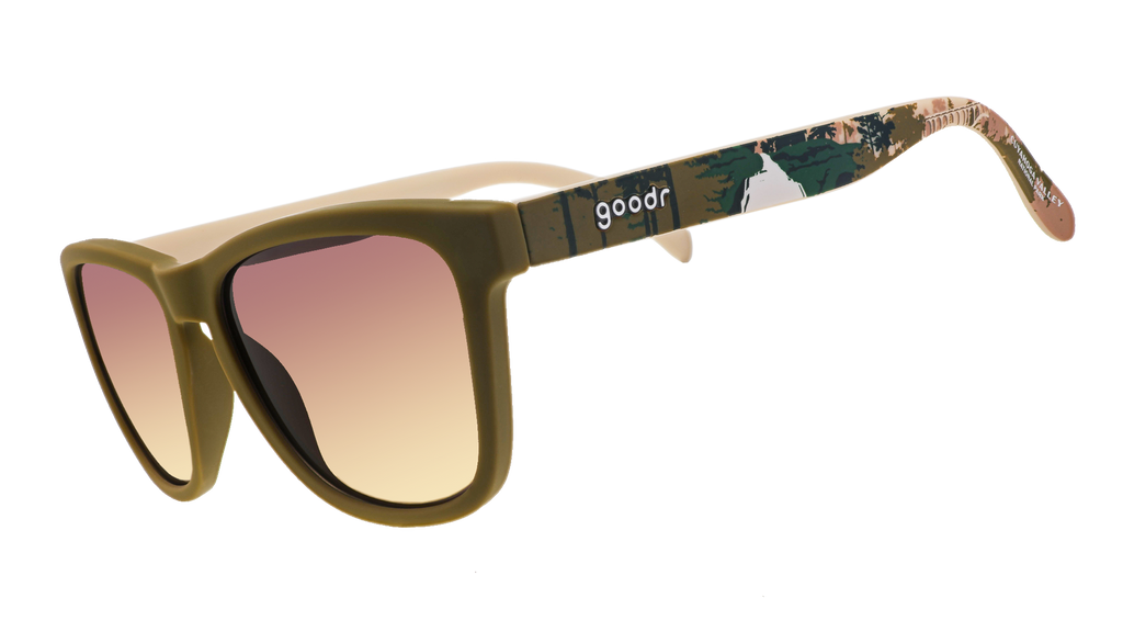 A pair of olive-green "goodr" sunglasses featuring gradient brown-tinted lenses and camouflage-patterned arms.