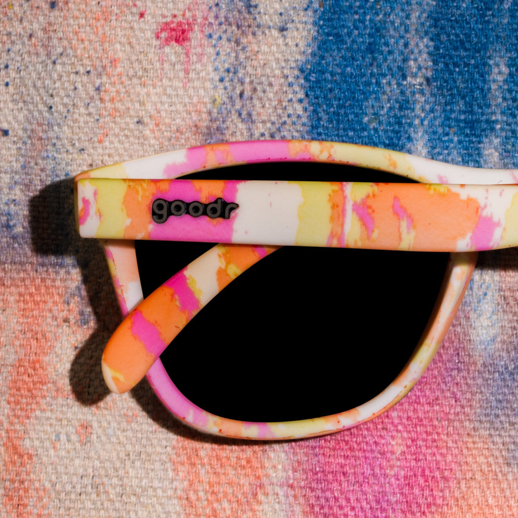 Close-up shot of cheery yellow tie-dye sunglasses photographed from behind, sitting on a vibrant tie-dye fabric backdrop.