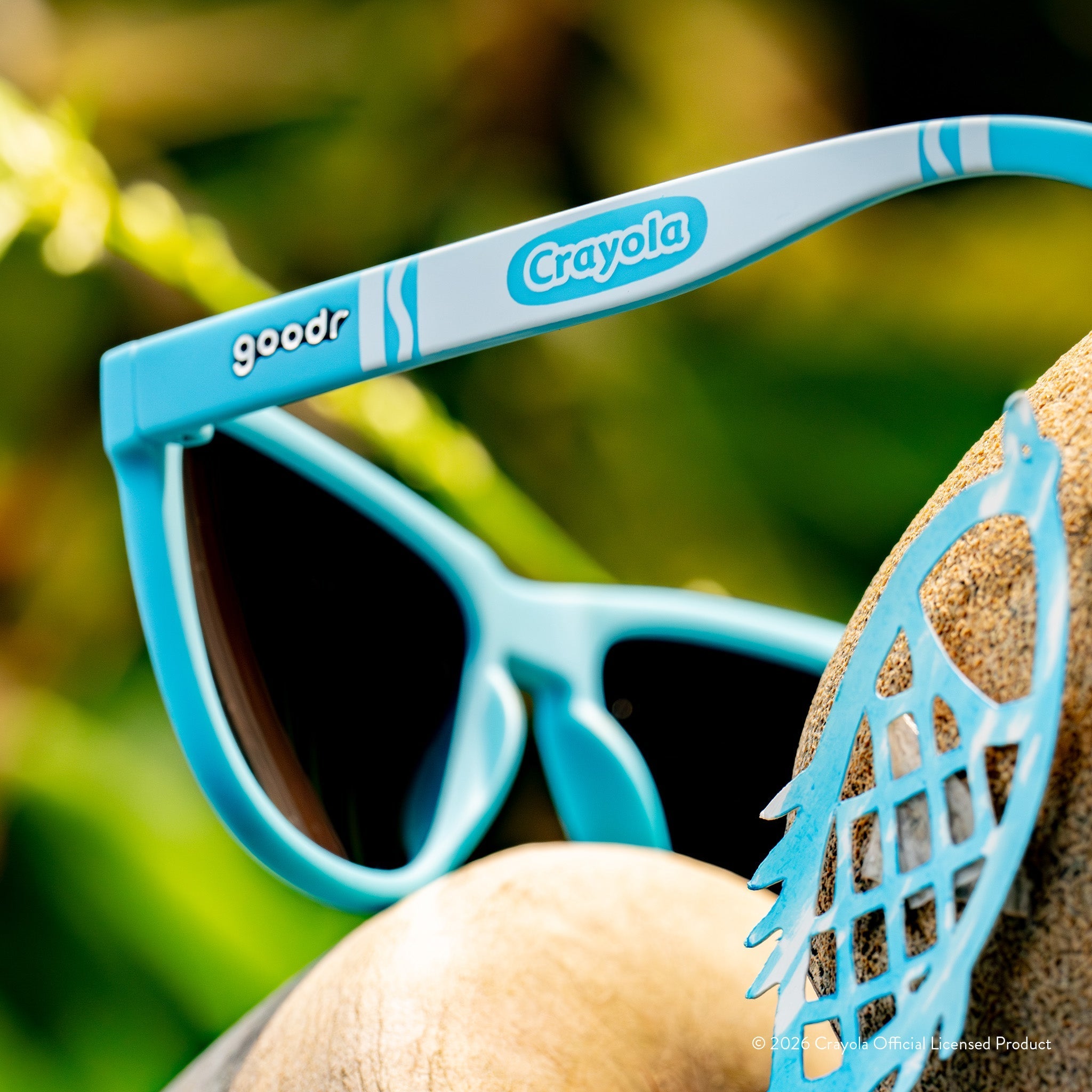 Angled close-up back view of blue shades w/ white Crayola marker pattern+blue reflective lenses on tropical background.