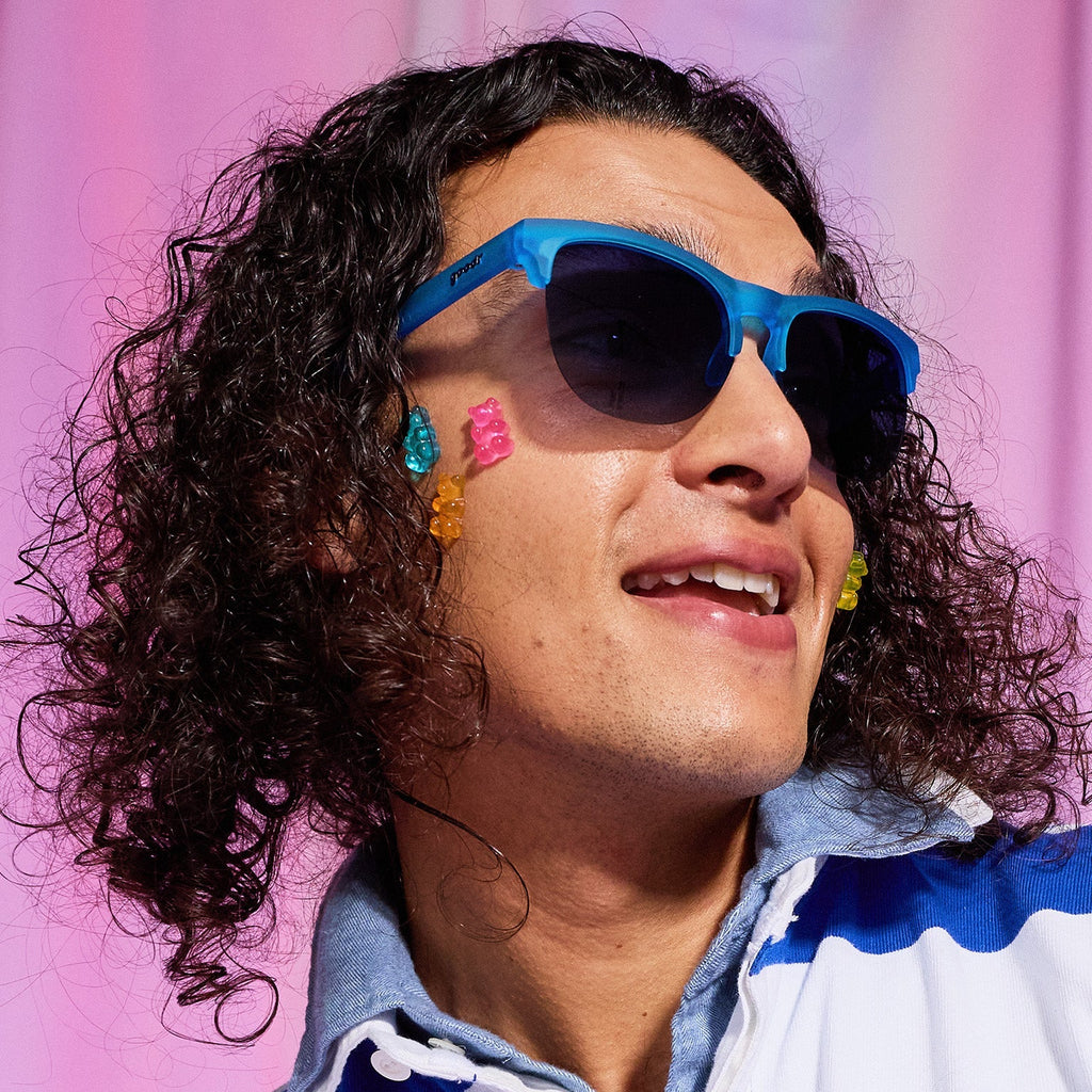 A man with dark curly hair and gummy bears stuck on his cheek wears translucent blue half-rim Avant G sunglasses.
