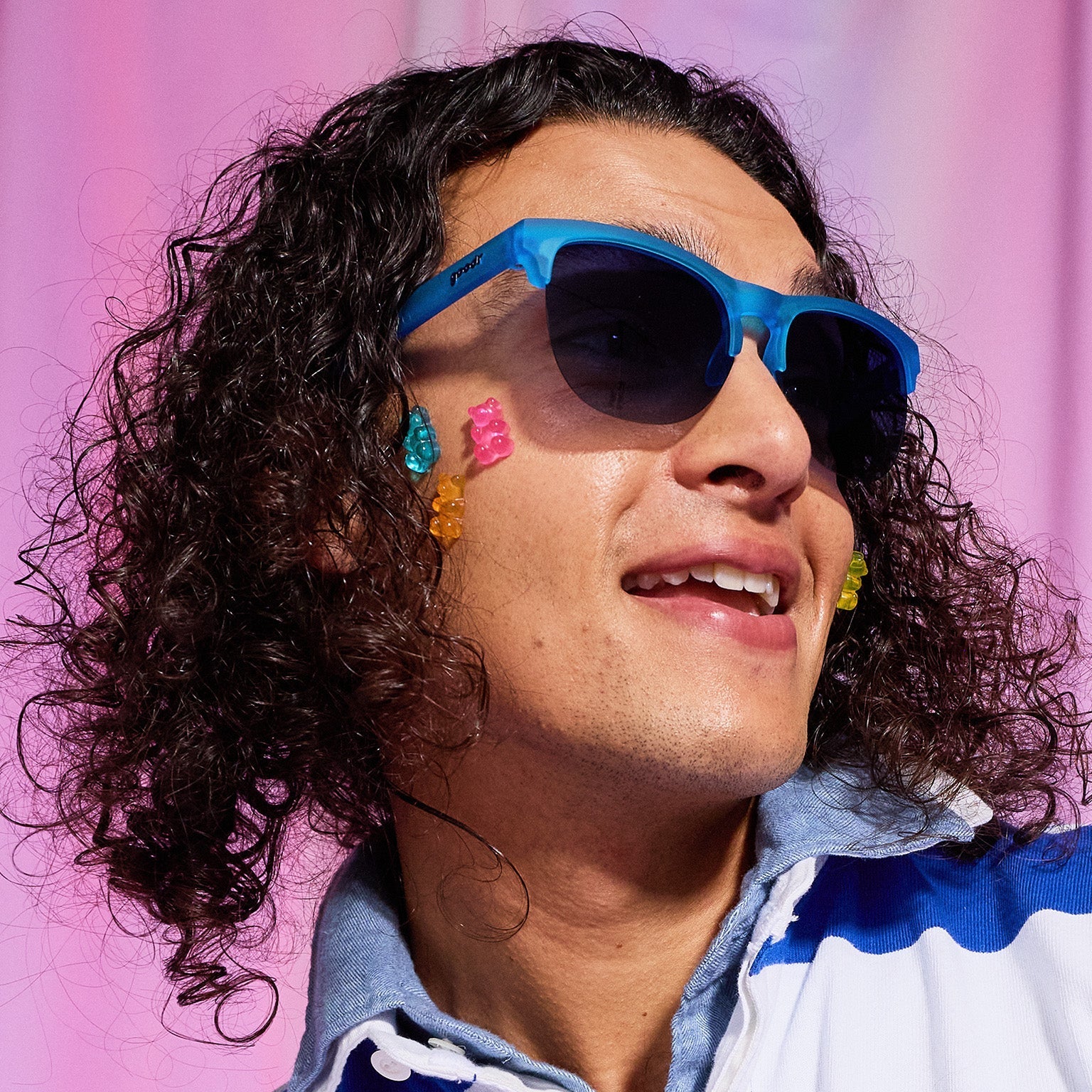 A man with dark curly hair and gummy bears stuck on his cheek wears translucent blue half-rim Avant G sunglasses.