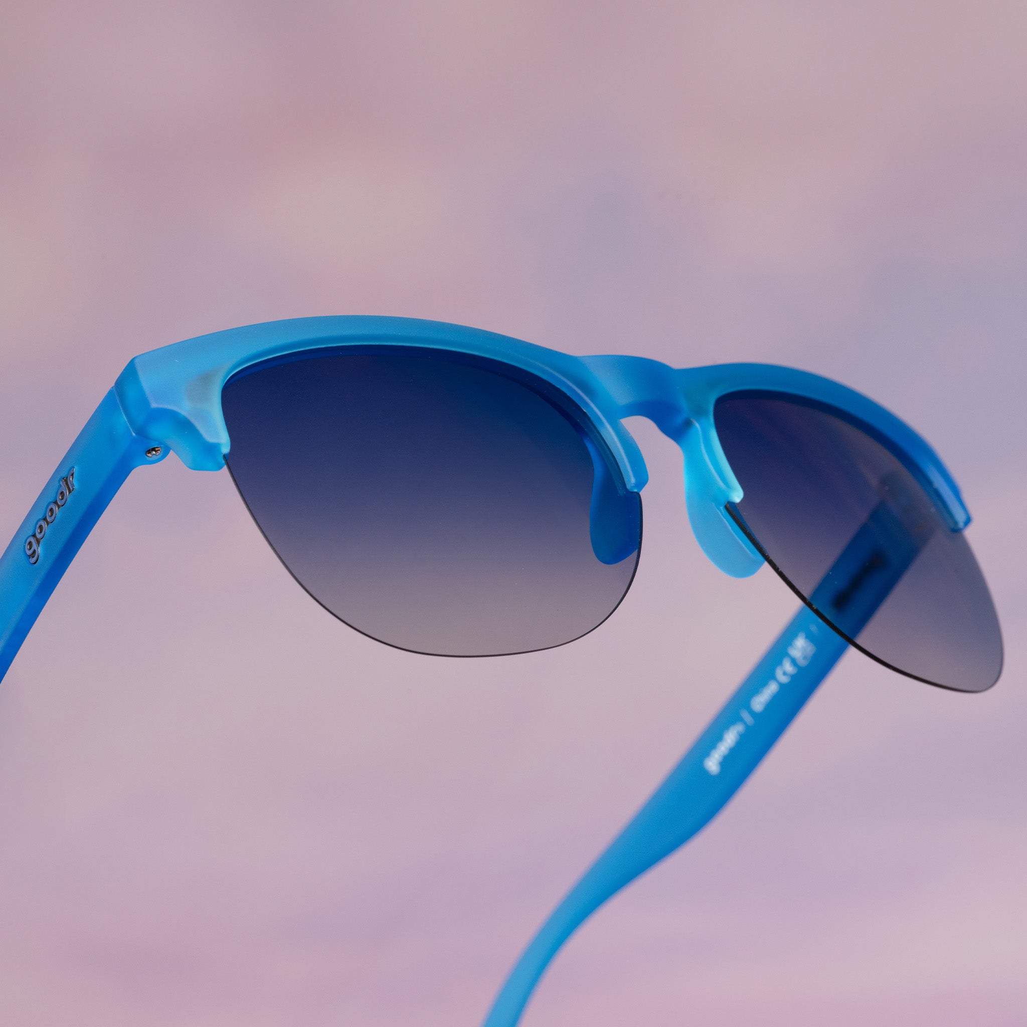 Three-quarter view of translucent blue half-rim Avant Gs with blue gradient lenses floating against a purplish pink backdrop.