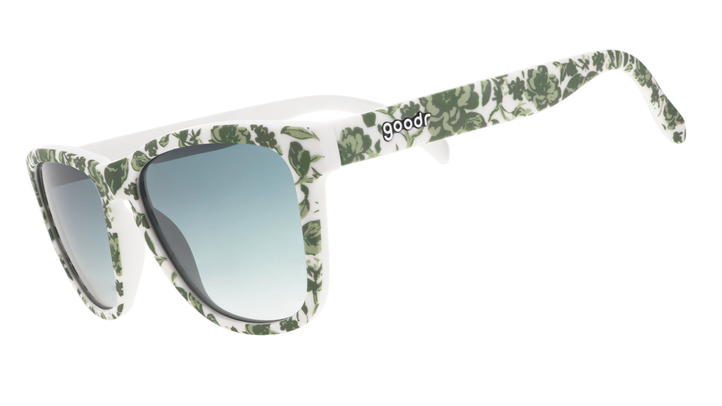 Three-quarter angle view of sunglasses with a green and white floral toile and green gradient lenses.