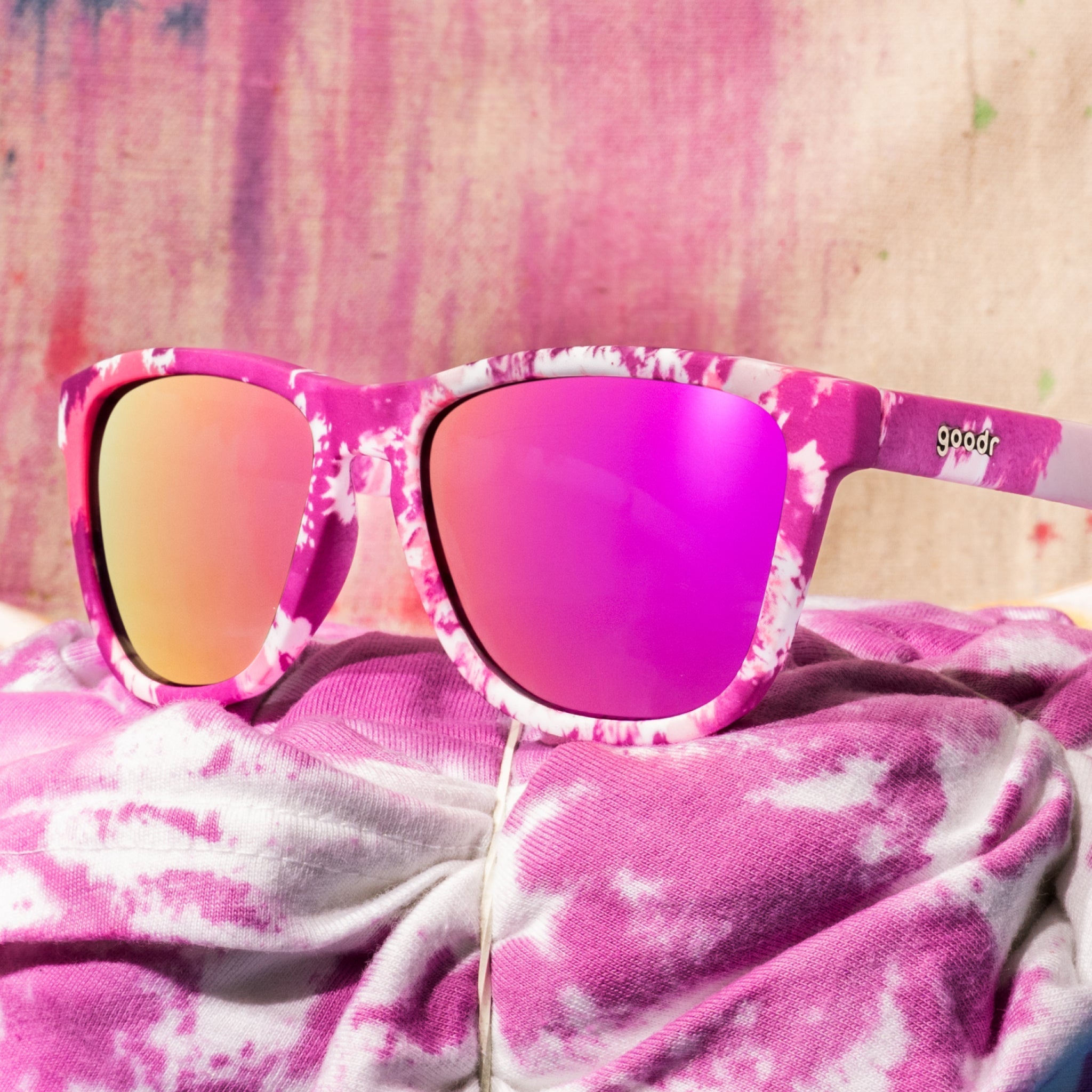 Purple tie-dye sunglasses sitting on white fabric tied with rubber bands, in the process of being tie-dyed with purple.