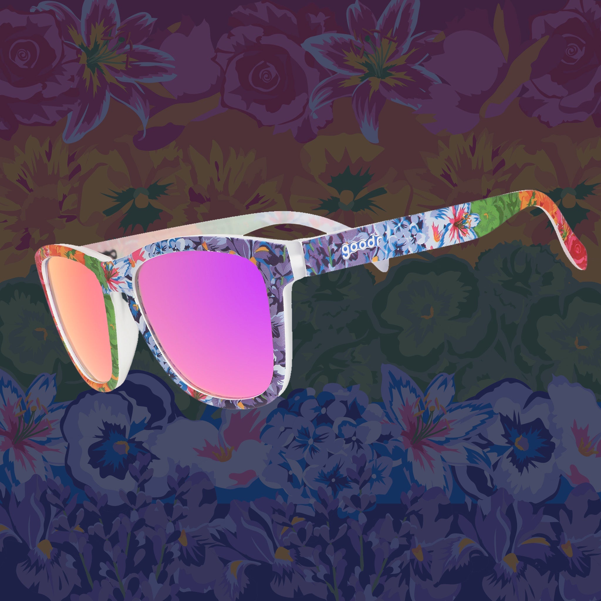Three-quarter angle view of colorful floral print goodr sunglasses with purple reflective lenses against a floral background.