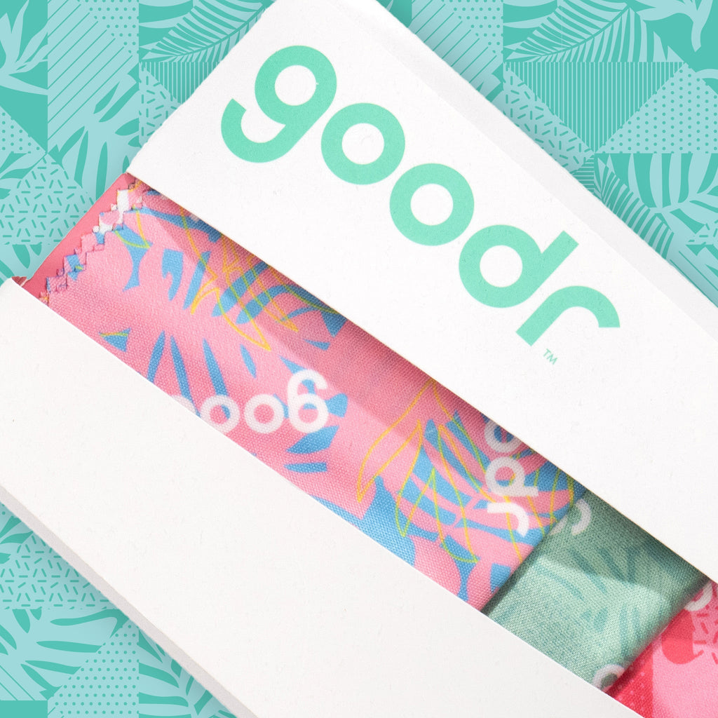 Close-up of a white box housing a pack of three tropical microfiber lens cloths in shades of pink and teal.