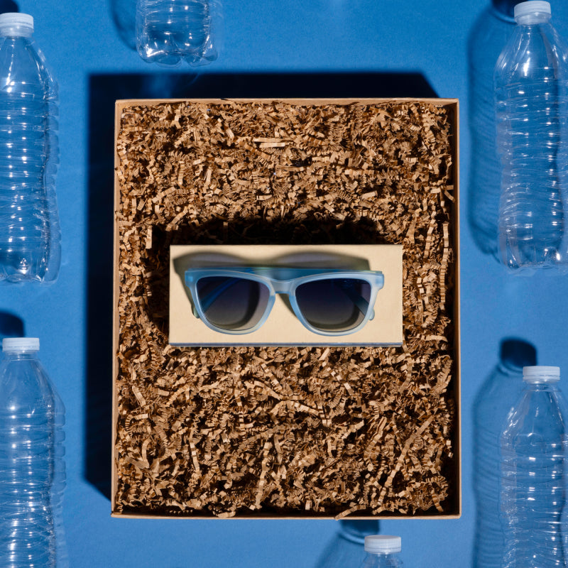 Angled view of translucent light blue sunglasses with 100% recycled plastic frames on crushed plastic bottles.