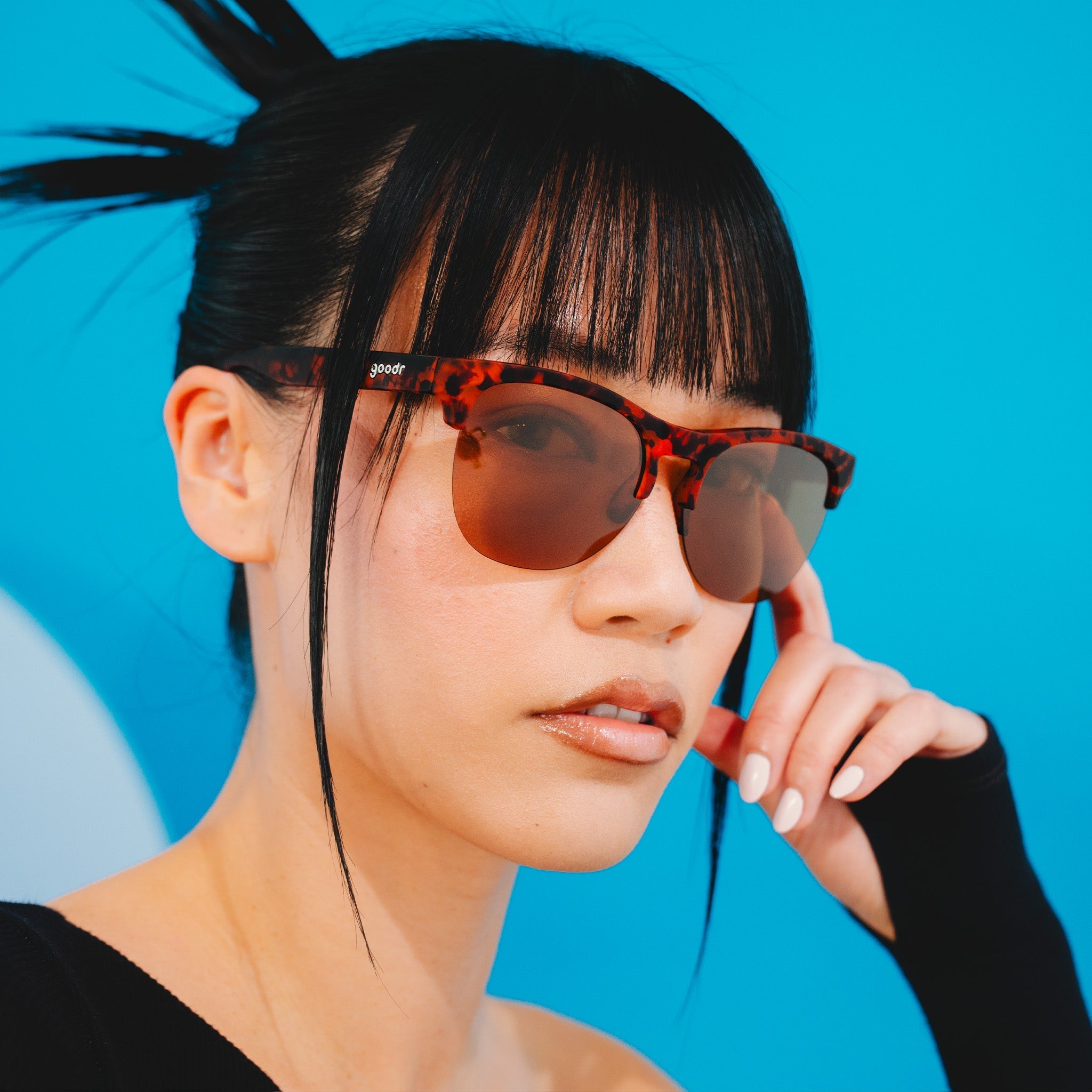 A stylish woman wearing brown tortoiseshell half-rim sunglasses with brown non-reflective lenses poses for the camera.
