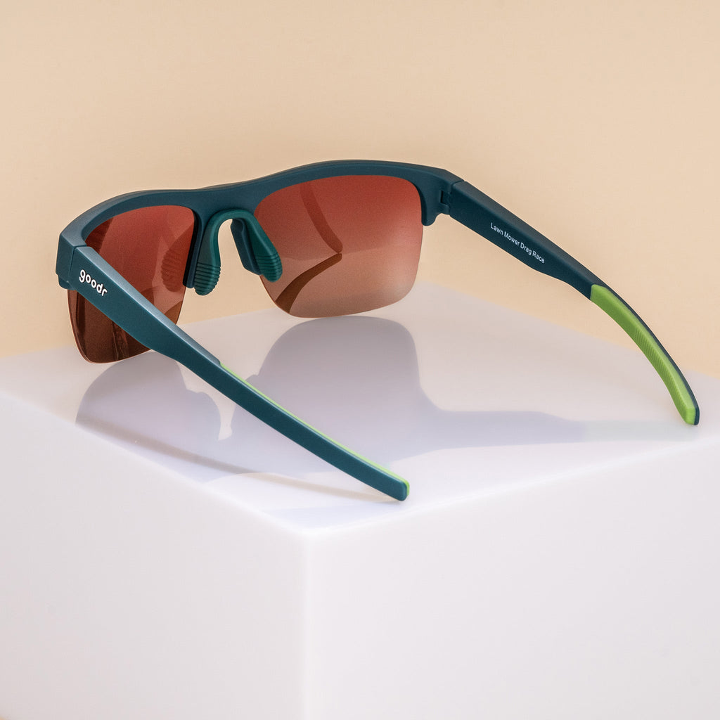 Three-quarter back angle view of solid green half-rim sunglasses with rose gradient lenses. The arms are extended, showcasing the goodr logo on the outer left arm, an adjustable silicone nose piece, and lime green silicone grips on the inner arms.