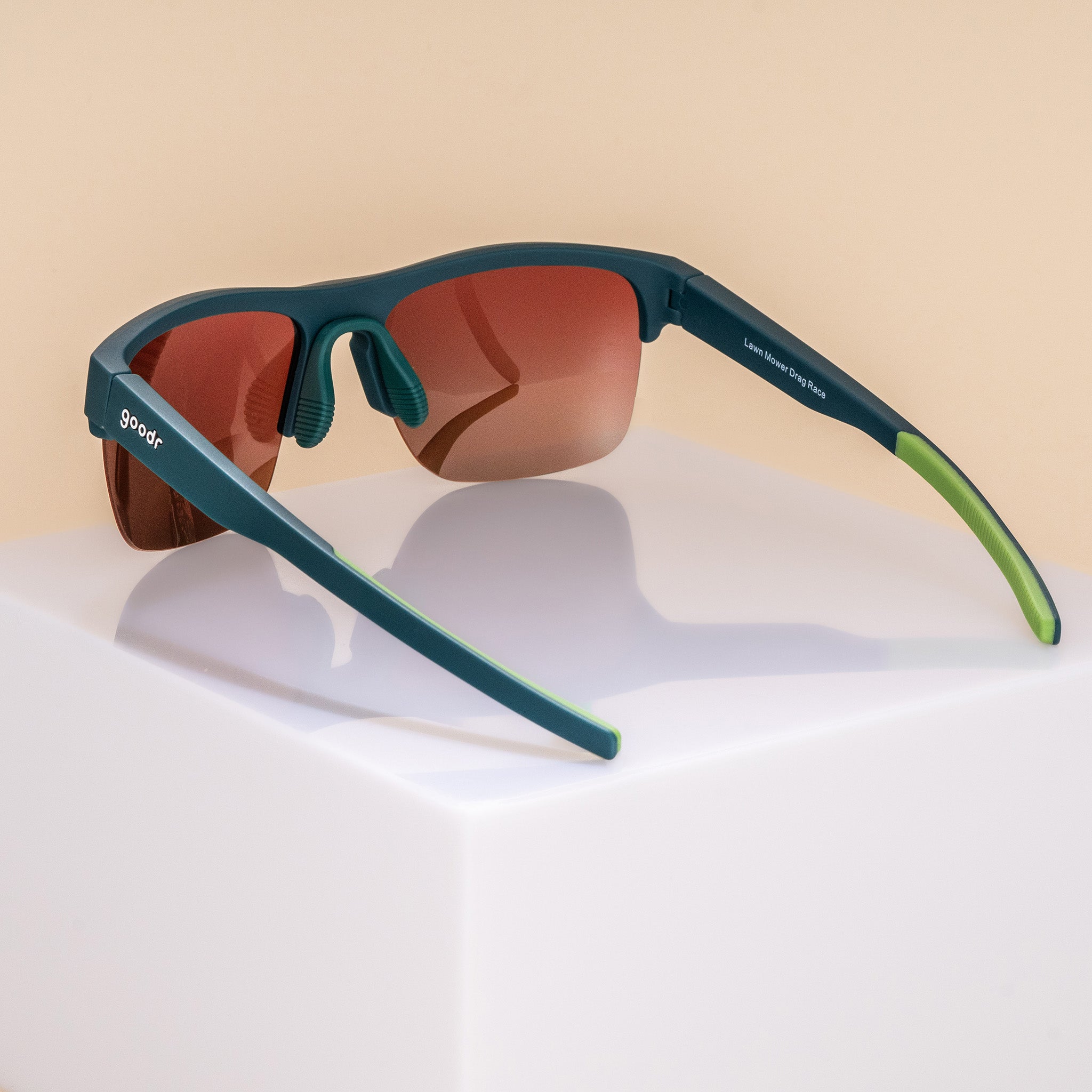 Three-quarter back angle view of solid green half-rim sunglasses with rose gradient lenses. The arms are extended, showcasing the goodr logo on the outer left arm, an adjustable silicone nose piece, and lime green silicone grips on the inner arms.