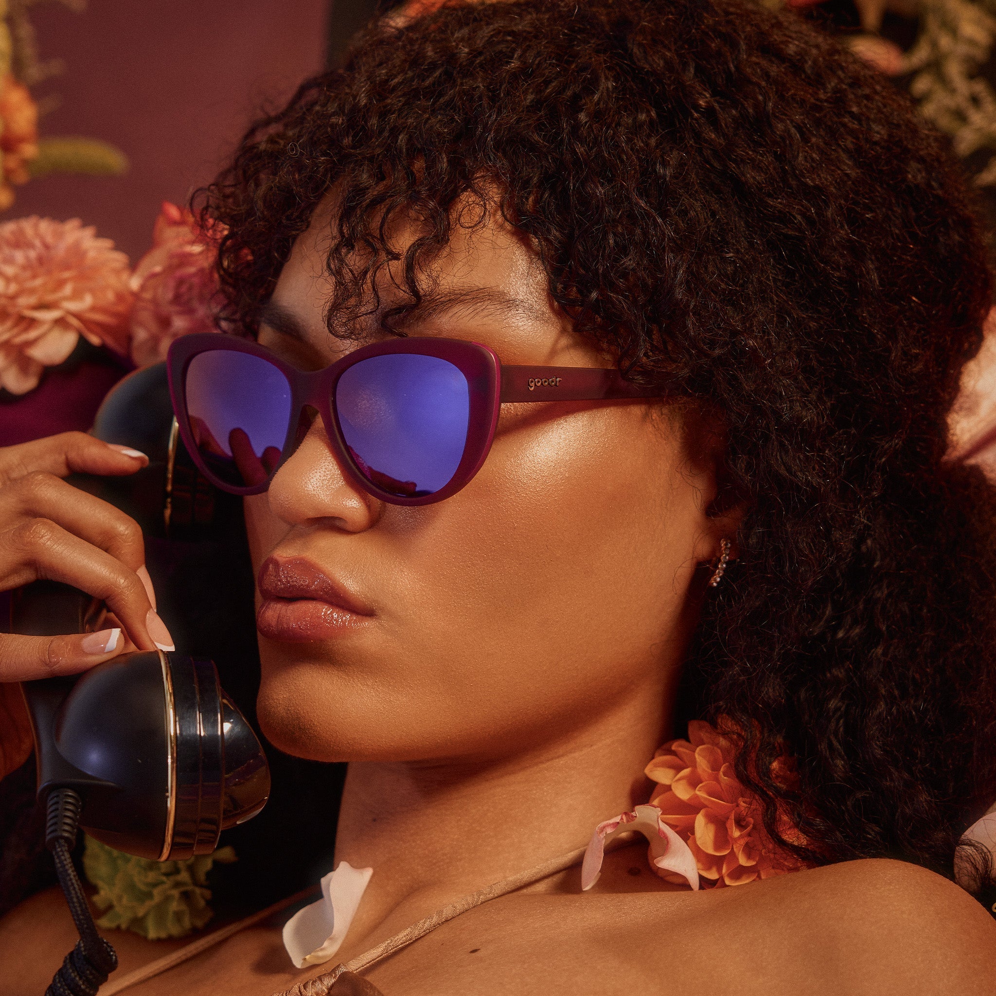 A woman on the phone poses in translucent purple cat-eye sunglasses with purple reflective lenses.