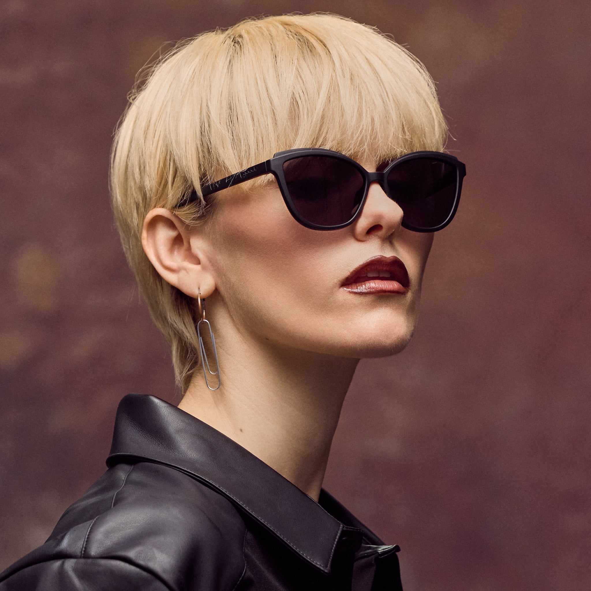 Woman wearing sunglasses and a black leather jacket against a brown background