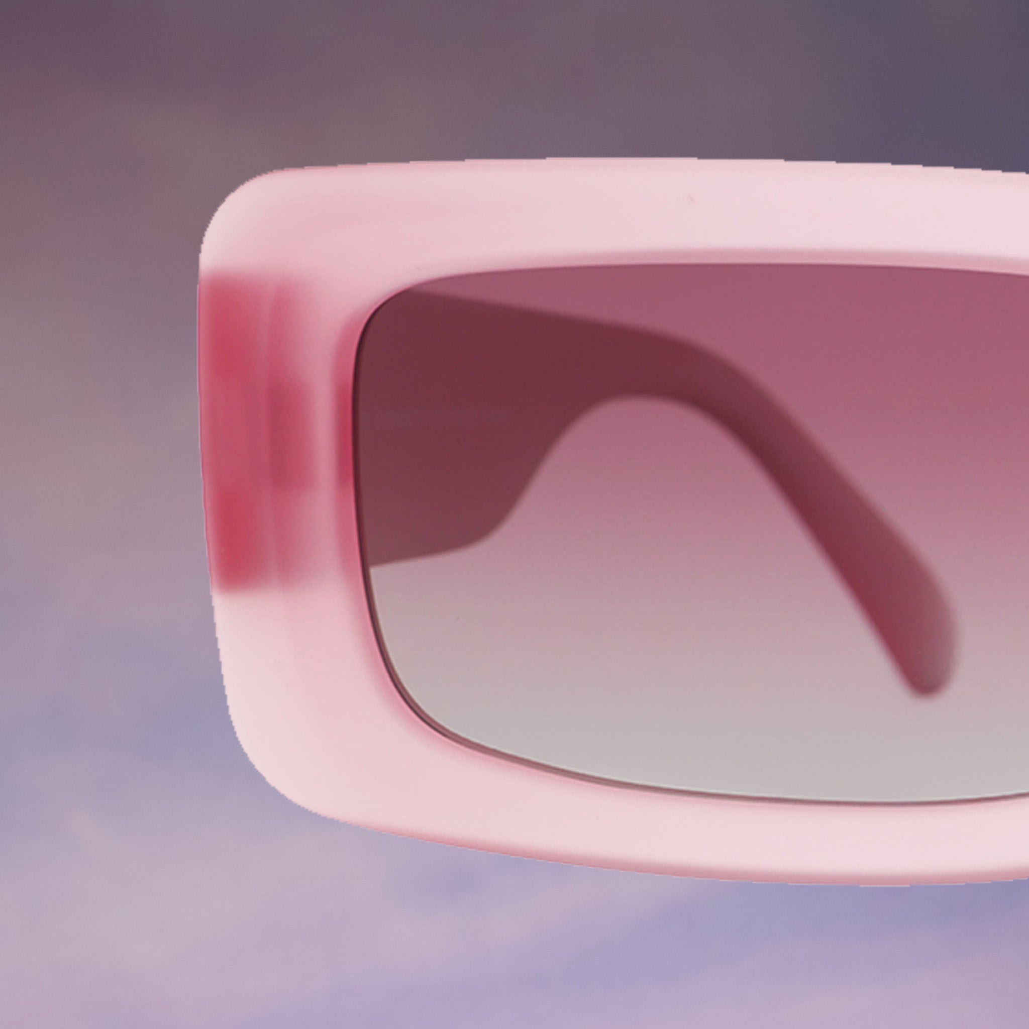 A close-up, front angle of the temple corner of a pair of translucent pink Luxe Gs against a purplish cloud-like backdrop.