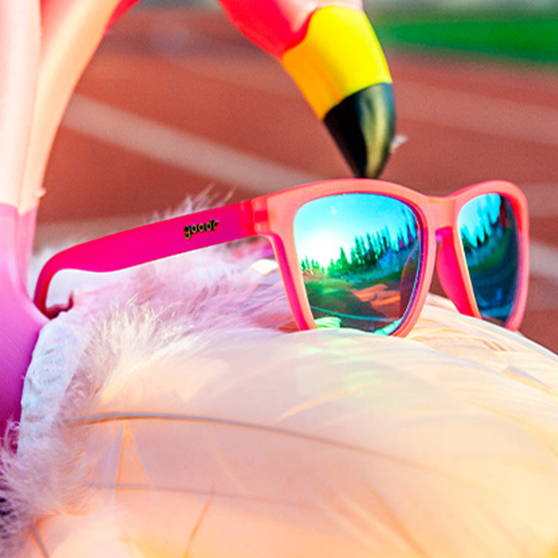 Three-quarter angle view of pink sunglasses with teal reflective lenses sitting atop an inflatable flamingo-shaped pool floatie.
