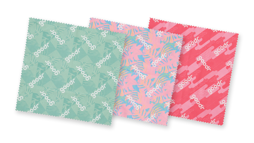 Close-up of a pack of three tropical microfiber lens cloths in shades of pink and teal on a teal, geometric tropical backdrop.