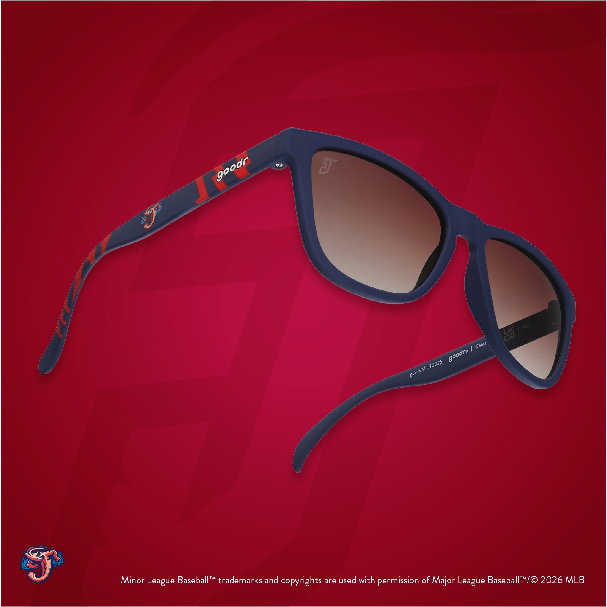 Three-quarter angle view of shades tilted up. Blue + red frames w/ Jumbo Shrimp logo on temples. Brown gradient lenses.