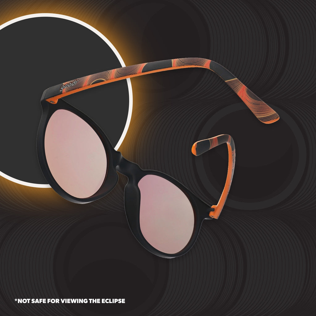 Back view of orange and black round sunglasses with reflective orange lenses in front of a gray background.