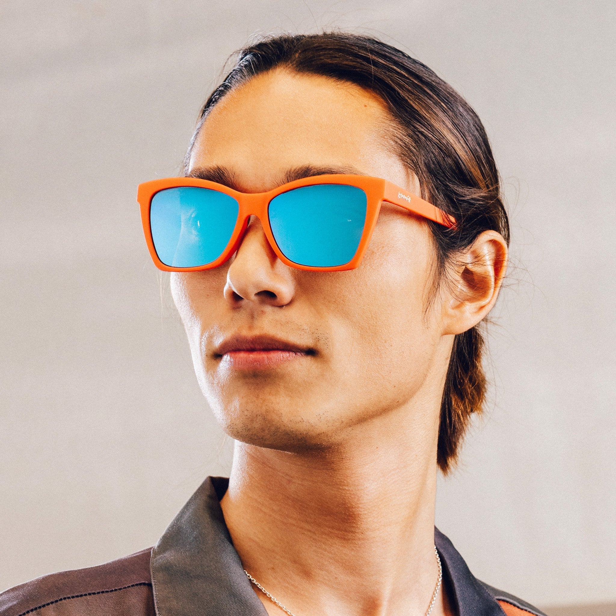 Man poses while wearing red angular sunglasses with blue reflective lenses.