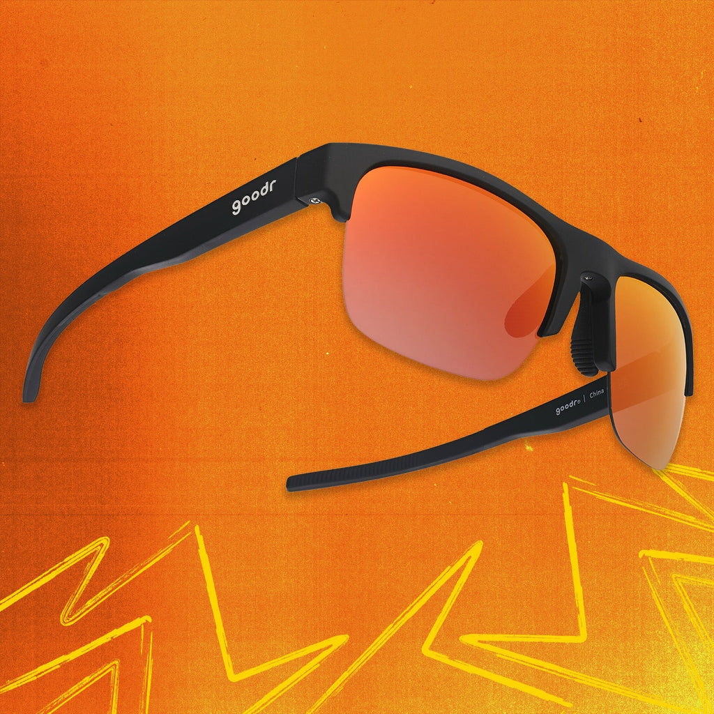 Three-quarter angle view of black shades w/ half-rim frames+orange reflective lenses tilted up on an orange background.