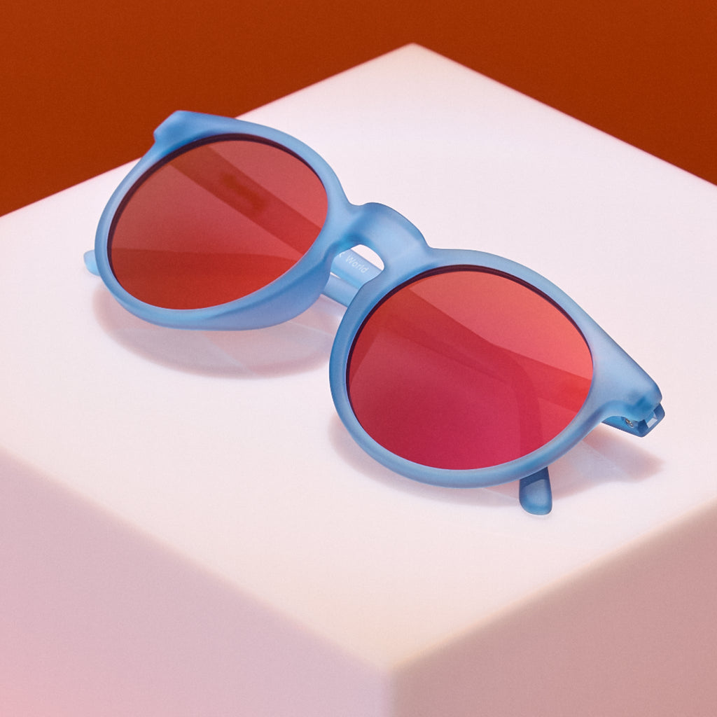 Blue sunglasses with red lenses on a white surface with a brown background