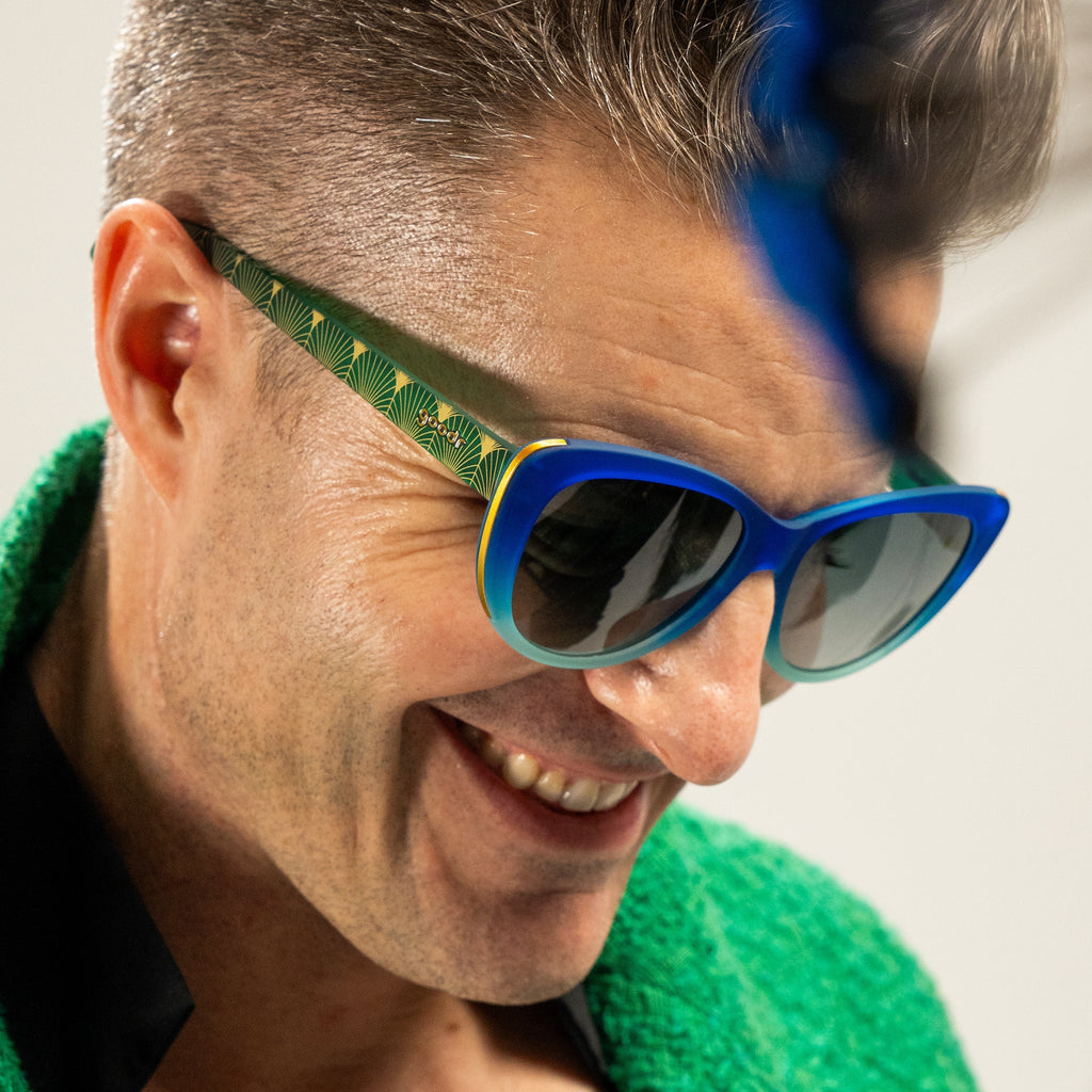 goodr's CEO smiling in blue and green ombré cat-eye frames with green gradient lenses and a peacock-inspired design.