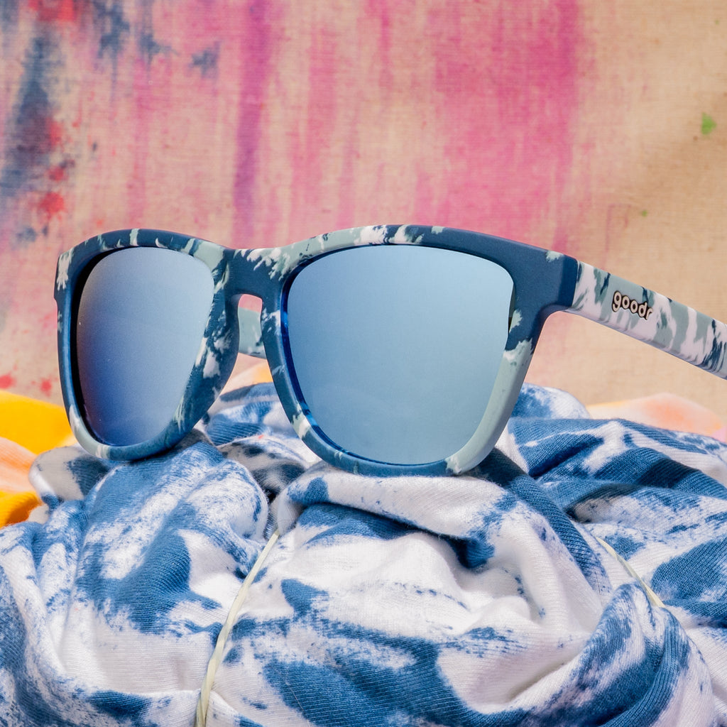 Close-up shot of blue tie-dye sunglasses photographed from behind, sitting on a moody tie-dye fabric backdrop.