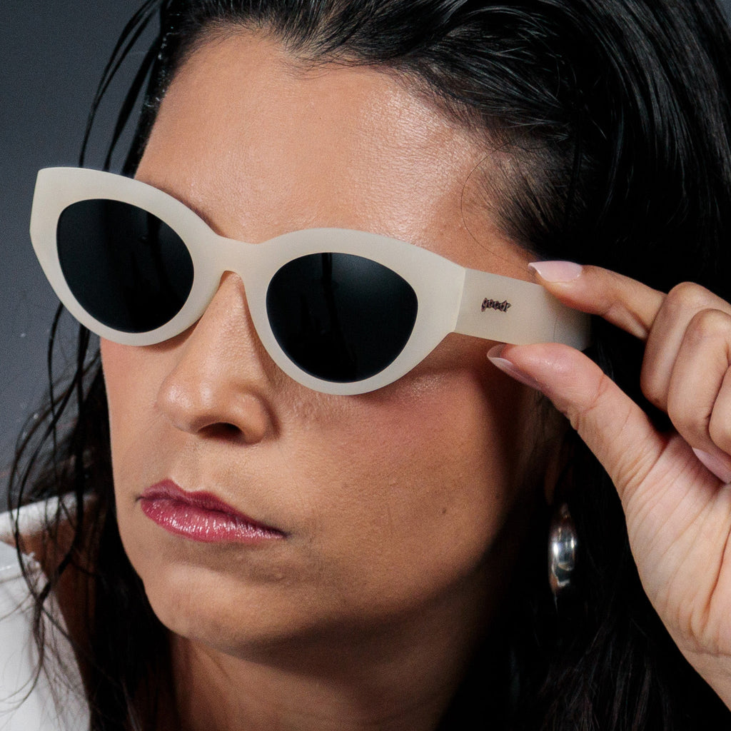 Three-quarter angle view of a woman wearing translucent soft cream, retro-inspired angled cat-eye sunglasses with black non-reflective lenses.