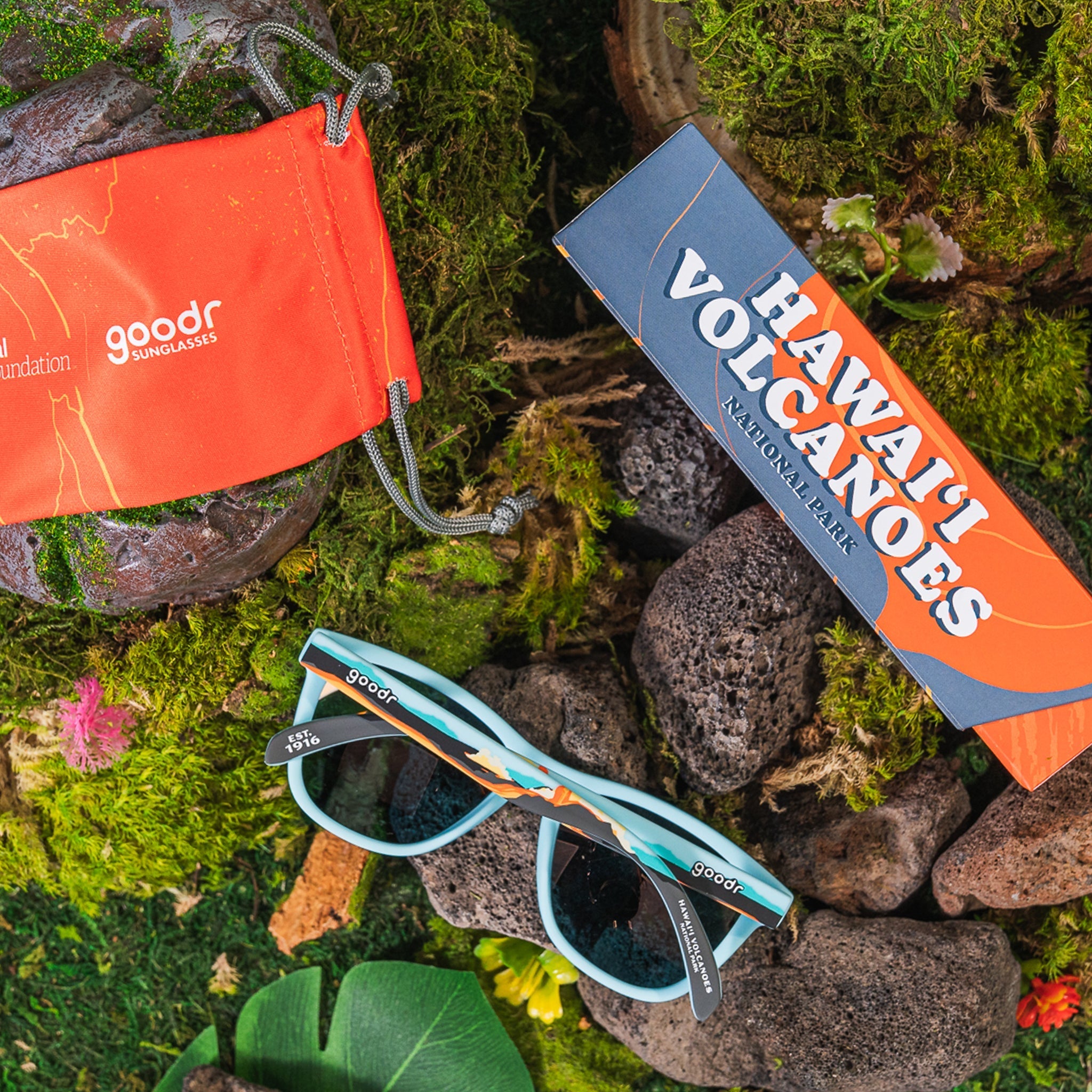 A pair of blue sunglasses sitting outside on some rocks, next to a case that reads "Hawai'i Volcanoes National Park"