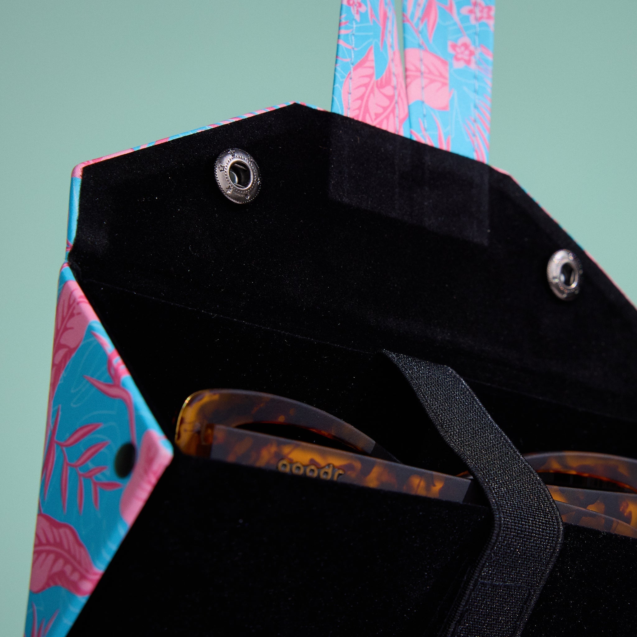 Close-up of silver-toned metal snaps that hold the case shut. A pair of tortoiseshell shades is shown secured inside the case by a black strap.