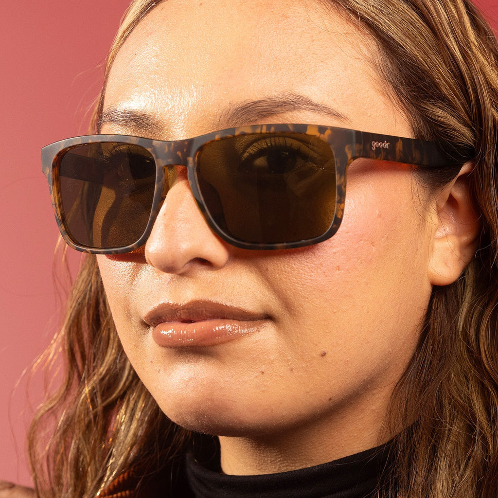 A stylish woman with wavy blonde hair looks at the camera brown tortoiseshell Grand Gs with brown non-reflective lenses.
