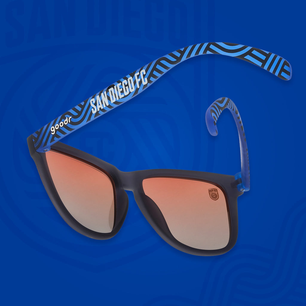 Back view of shades tilted down. Dark gray frames w/ blue waves, San Diego FC on temples+orange gold gradient lenses.