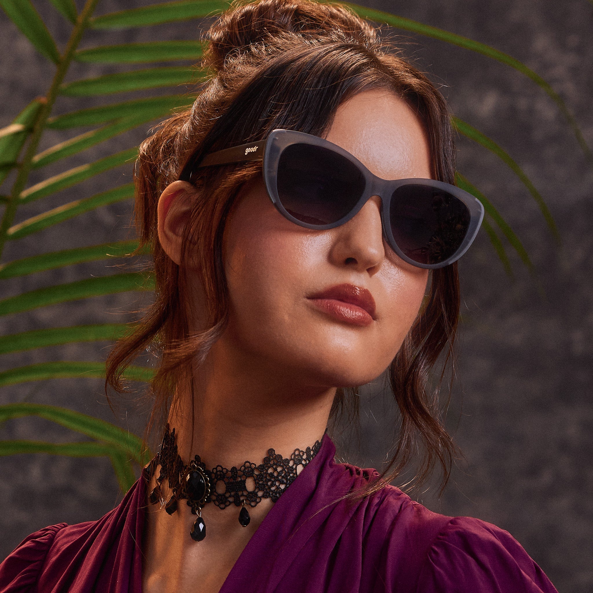 An elegantly dressed woman in translucent gray cat-eye sunglasses with black gradient lenses.