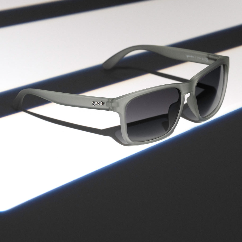 Three-quarter angle view of translucent gray Grand Gs with black gradient lenses on a dark gray striped surface.