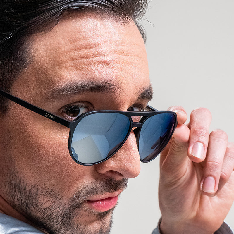 A man looks over his shoulder with black and chrome aviator sunglasses slid down his nose.