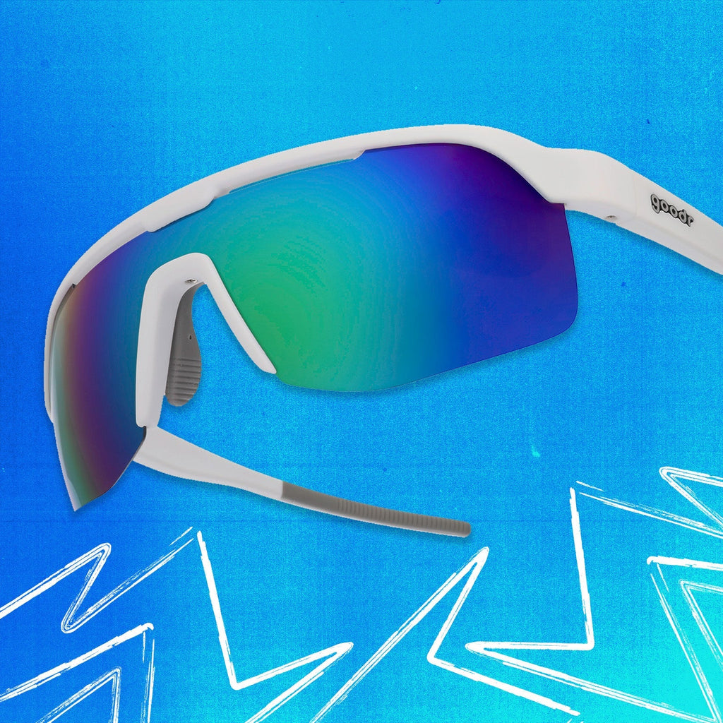 Three-quarter angle view of white shield sunglasses with green reflective wrap lenses tilted up on a blue background.