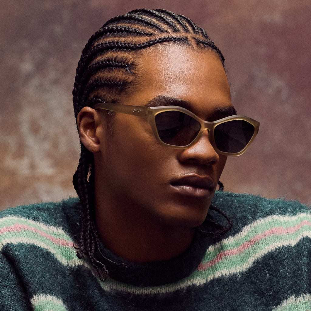Person wearing sunglasses and a striped sweater against a brown background