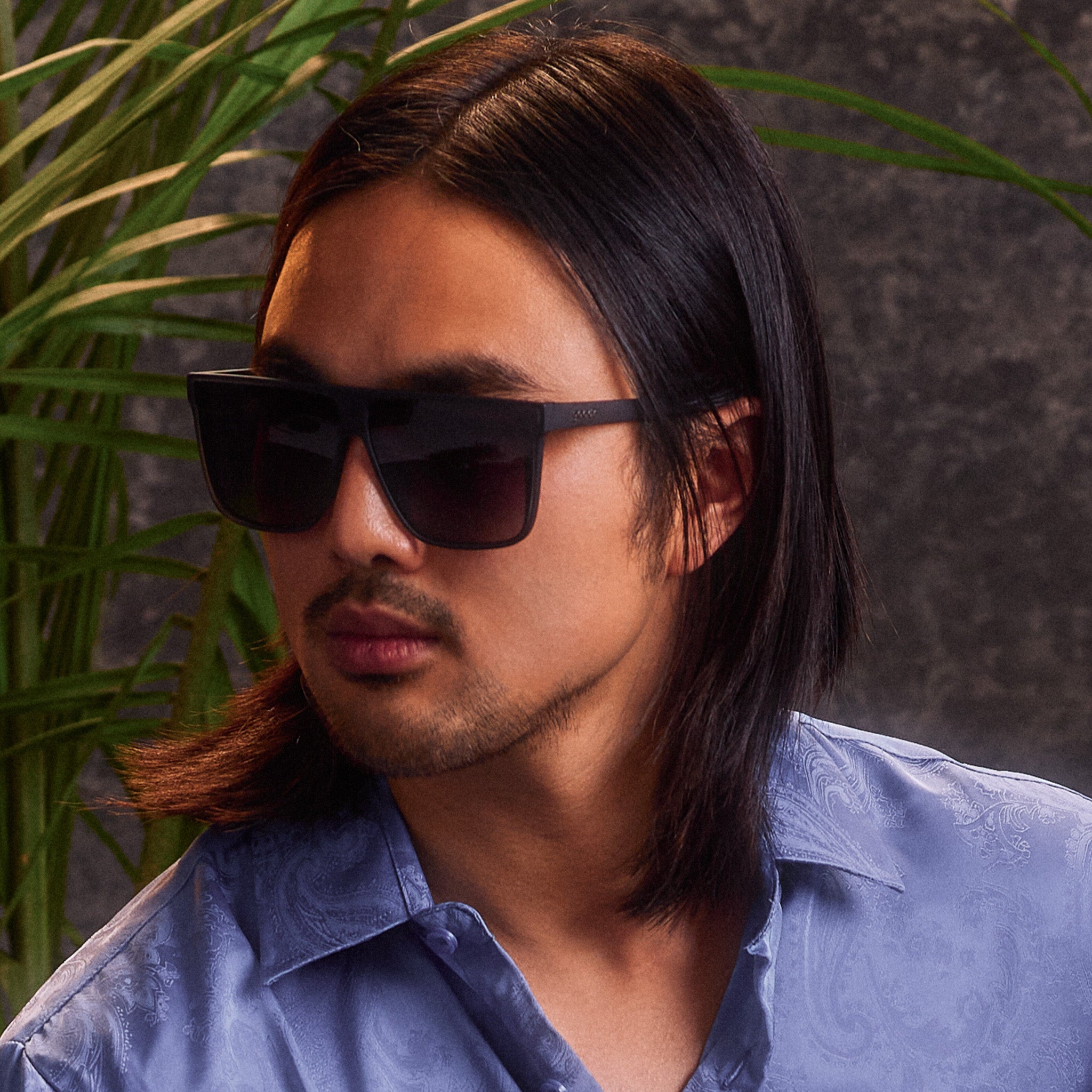 A young man with dark, shoulder-length hair poses in a pair of translucent gray, flat-top Fly Gs with gray gradient lenses.