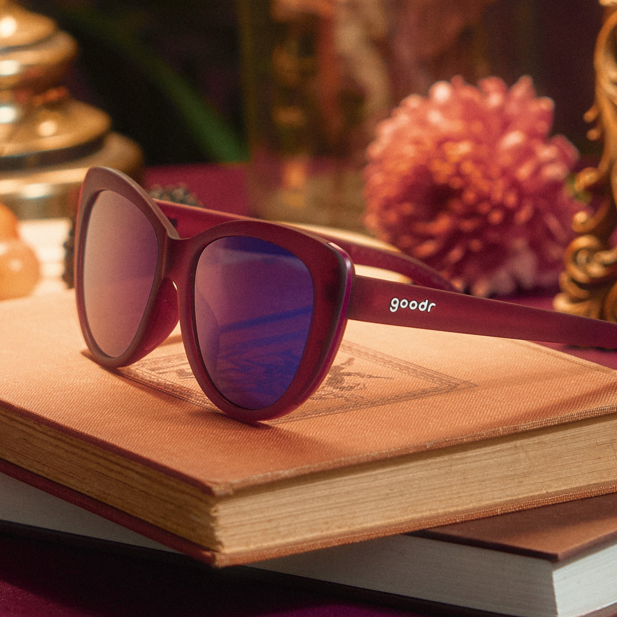 Three-quarter angle view of translucent purple cat-eye sunglasses with purple reflective lenses on top of stacked books.