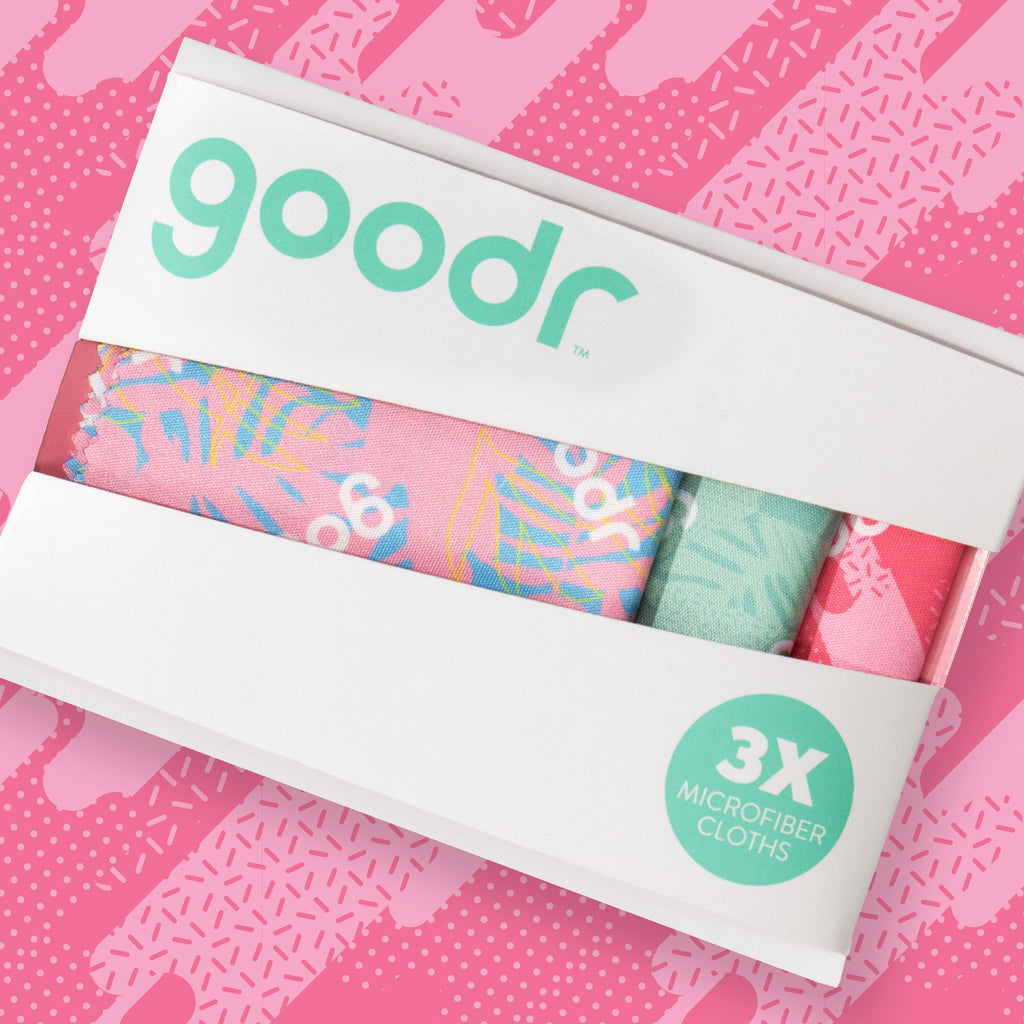 Front-facing shot of three square microfiber lens cloths with a geometric tropical print in shades of pink and teal.