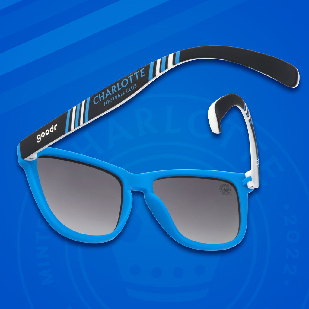 Three-quarter angle back view of MLS Charlotte FC shades on a blue background. Blue+black frames. Black gradient lenses.