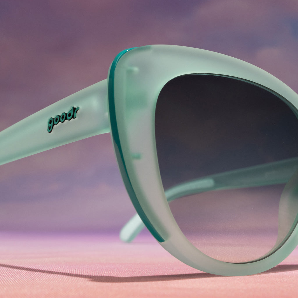 Close-up view of the temple of a pair of translucent pale green Glam G cat-eye sunglasses with green gradient lenses.