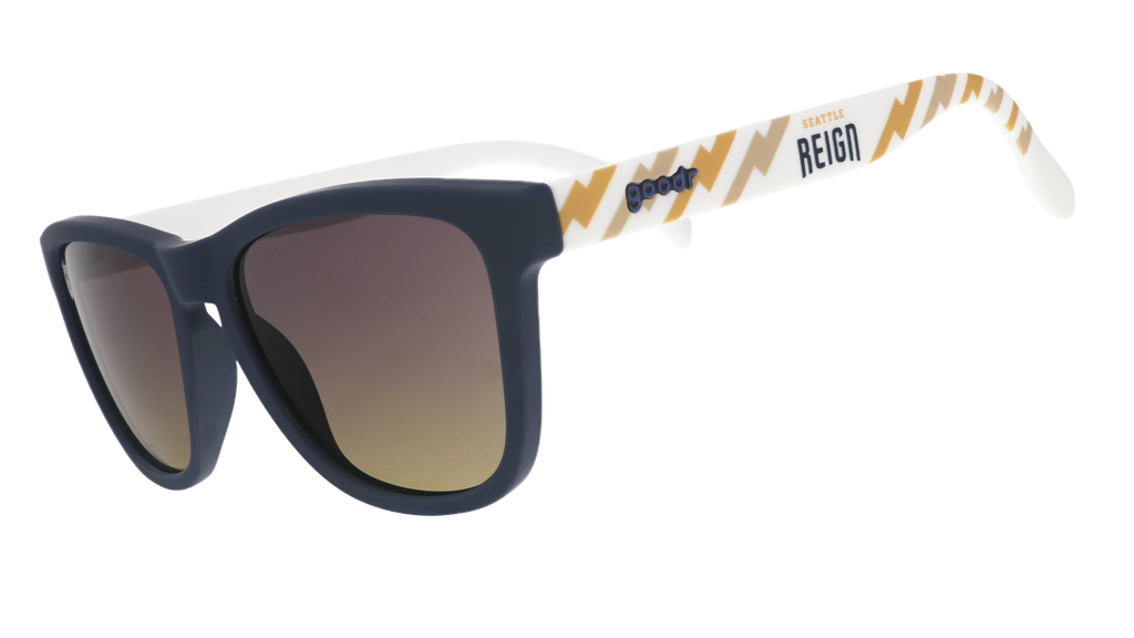 Three-quarter view of black and white sunglasses with a golden sunrise pattern, the Seattle Reign logo, and gray-to-yellow ocean gradient lenses.