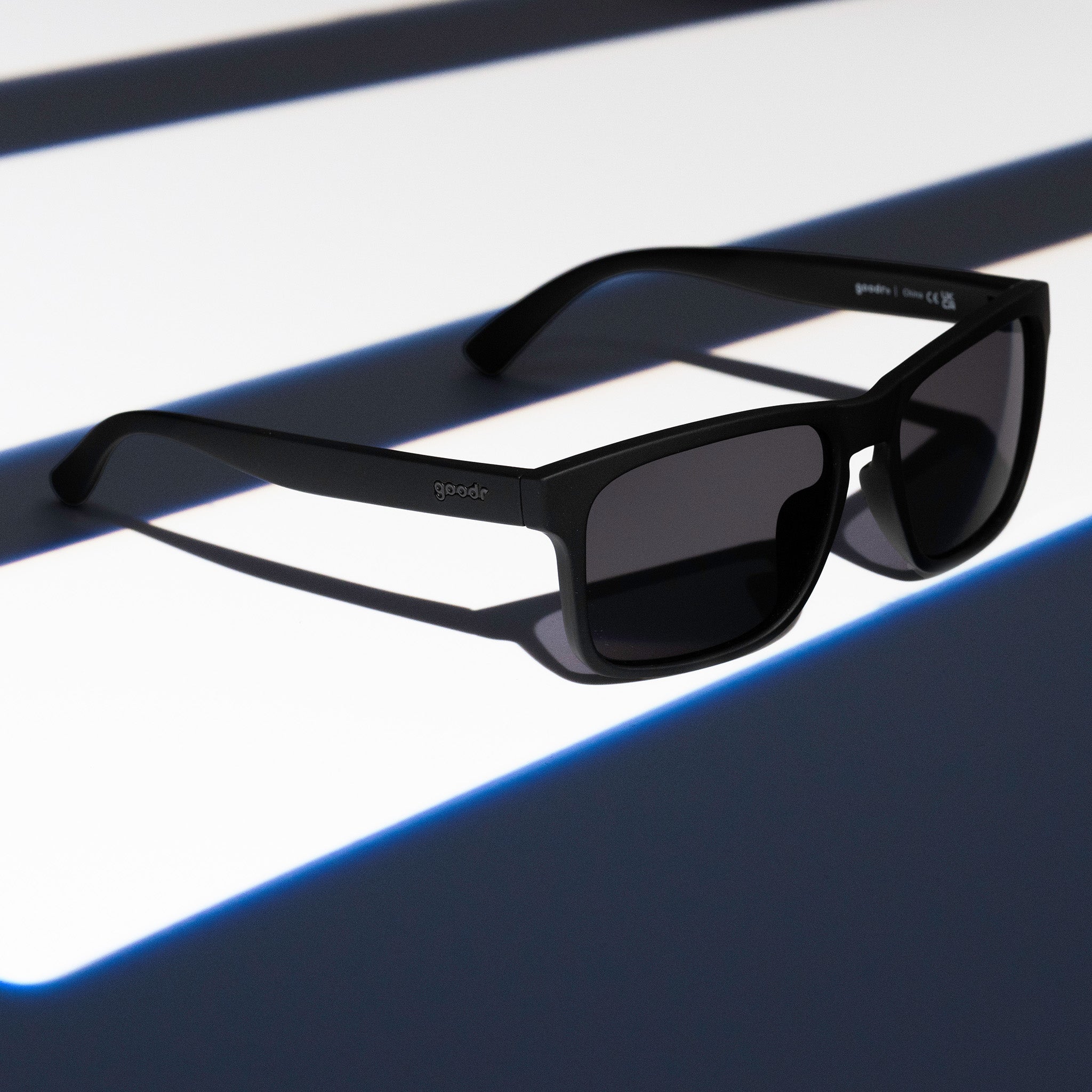 Three-quarter angle view of black Grand Gs with black non-reflective lenses on a black striped surface.
