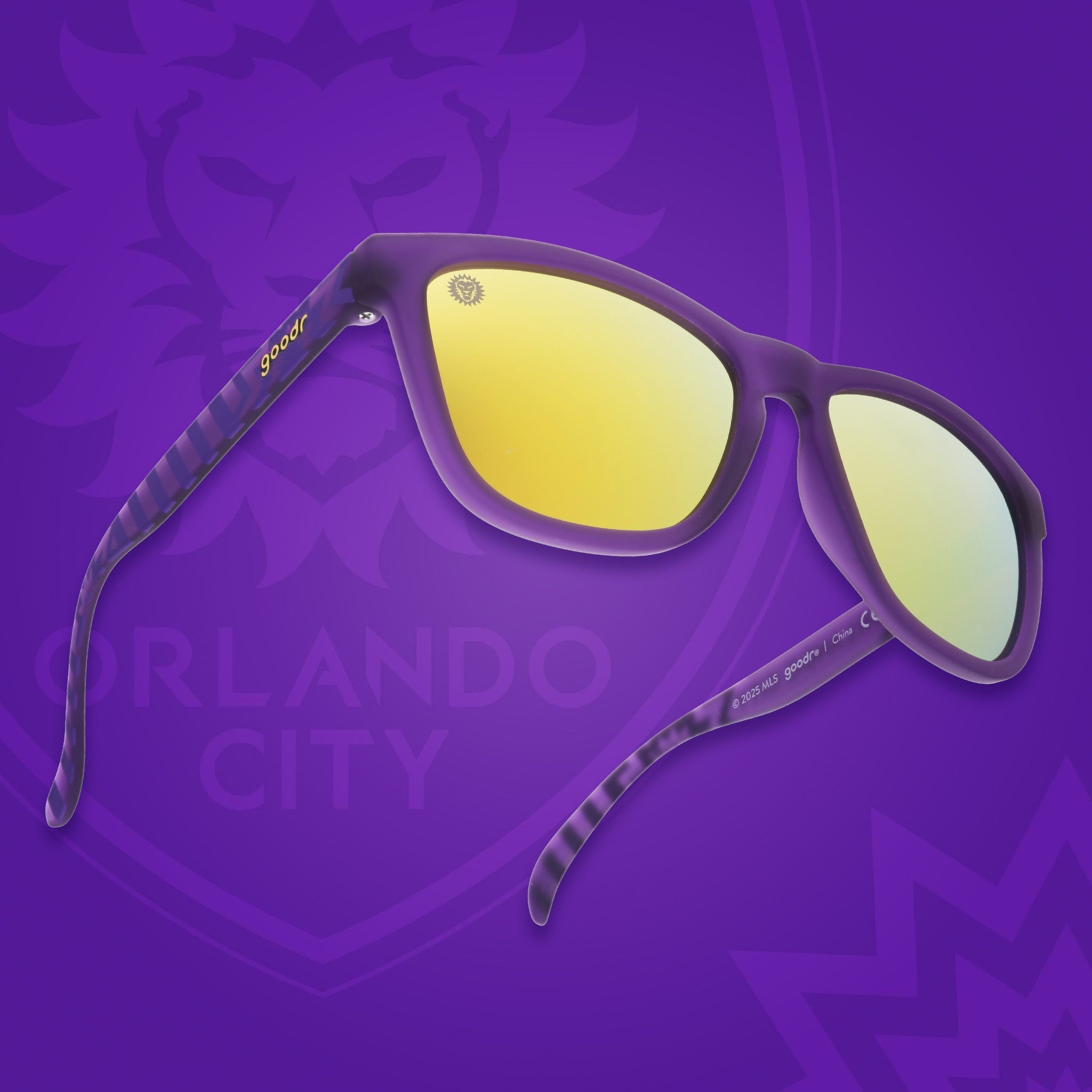 Angled view of shades tilted up. Purple frames w/ stripes + Orlando City on temples. Violet reflective lenses.