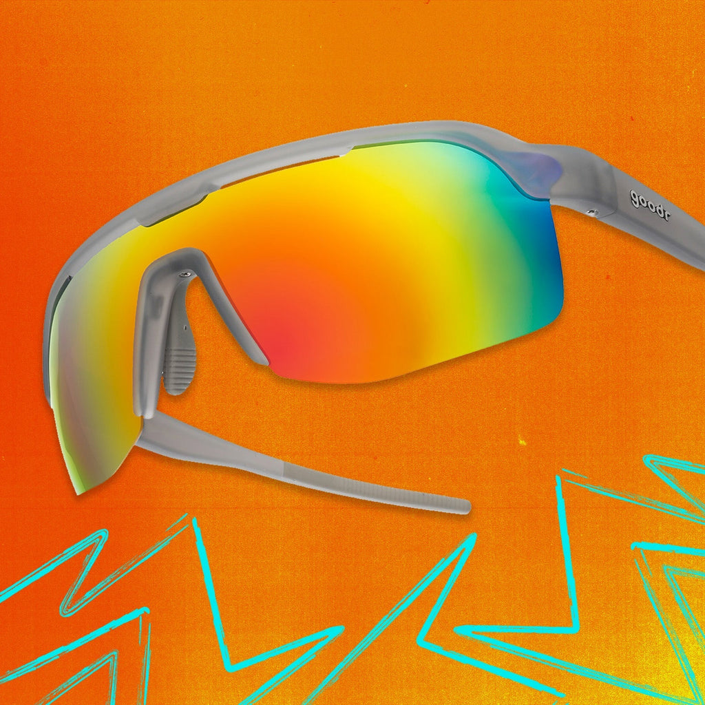 Three-quarter angle view of gray shield sunglasses with orange reflective wrap lenses tilted up on an orange background.