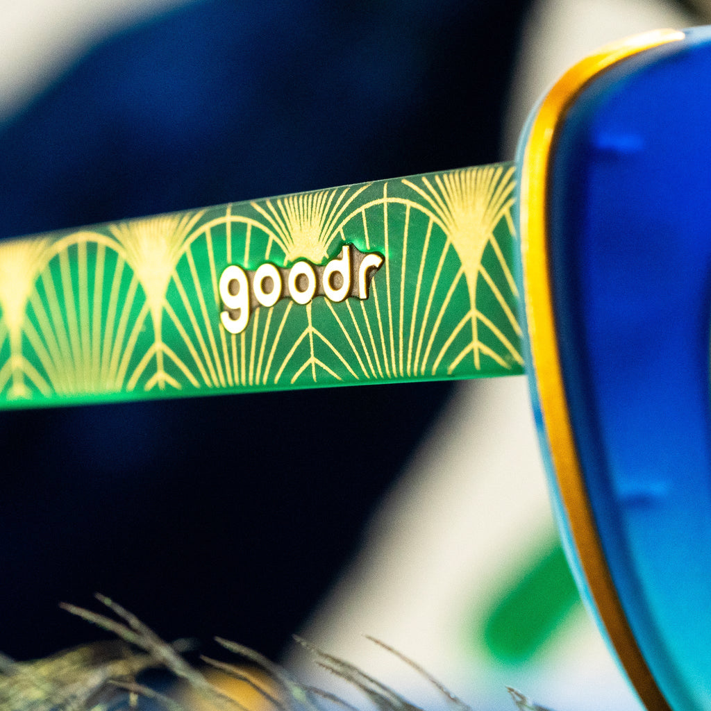 Close-up of temple of blue cat-eye frames with green gradient lenses, peacock-inspired design on the arms with gold accents.